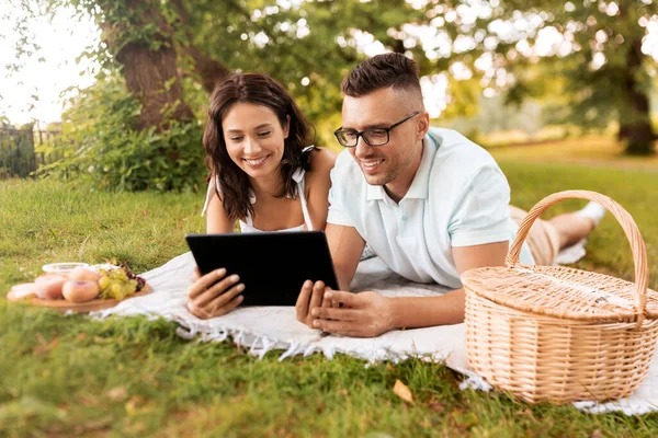 Lyckligt par med surfplatta på picknick i parken — Stockfoto