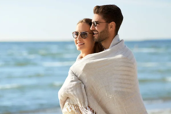 Lyckligt par täckt med filt kramas på stranden — Stockfoto
