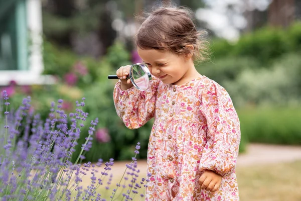 庭の花を見て拡大鏡を持つ女の子 — ストック写真