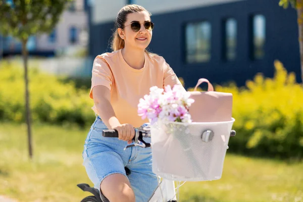 Woman with flowers in bicycle basket in city — Stock Photo, Image