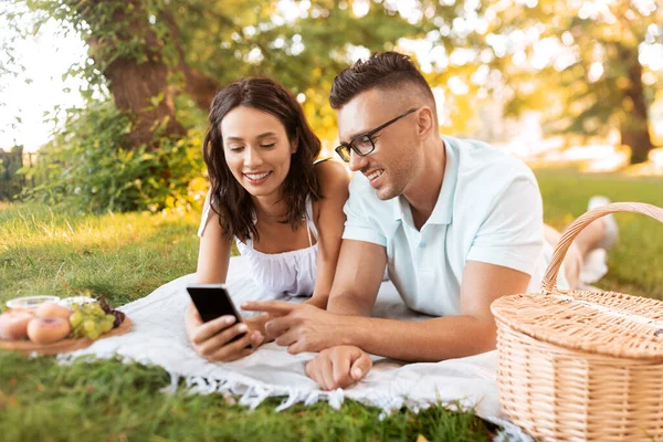 Pareja feliz con teléfono inteligente en el picnic en el parque —  Fotos de Stock