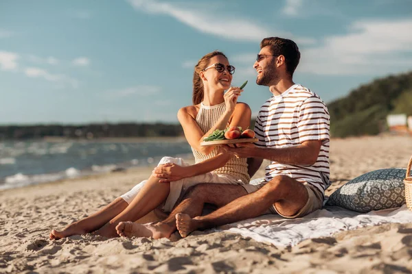 Glückliches Paar mit Essen beim Picknick am Strand — Stockfoto