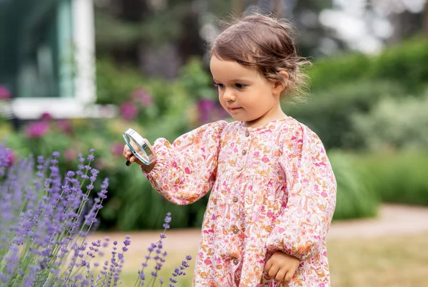 庭の花を見て拡大鏡を持つ女の子 — ストック写真