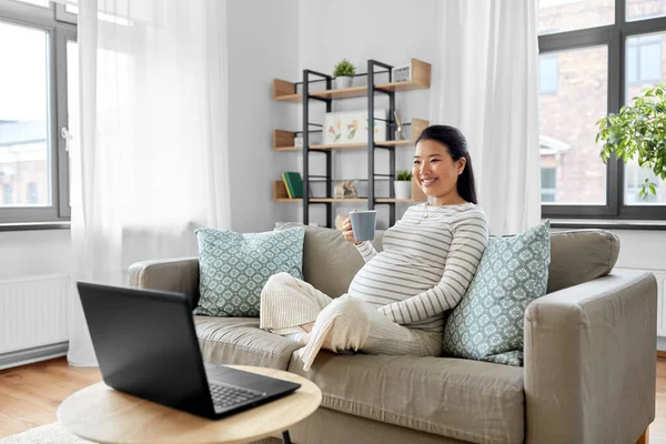 Ευτυχισμένη έγκυος Ασιάτισσα γυναίκα με φορητό υπολογιστή στο σπίτι — Φωτογραφία Αρχείου