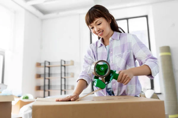 Vrouw met zelfklevende tape verpakking doos in nieuw huis — Stockfoto