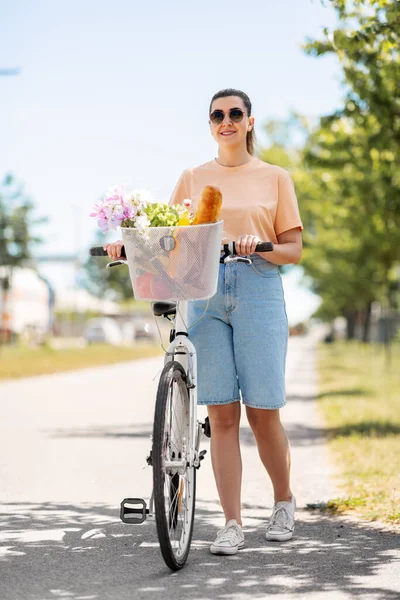 提着食物和鲜花在自行车篮子里的女人 — 图库照片