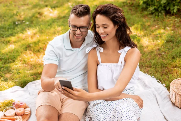 Šťastný pár s chytrým telefonem na pikniku v parku — Stock fotografie