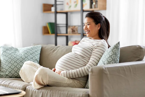 Gelukkig zwanger aziatische vrouw zitten op bank thuis — Stockfoto