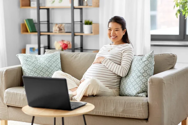 Ευτυχισμένη έγκυος Ασιάτισσα γυναίκα με φορητό υπολογιστή στο σπίτι — Φωτογραφία Αρχείου
