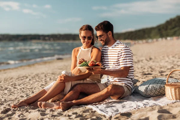 Glückliches Paar mit Essen beim Picknick am Strand — Stockfoto