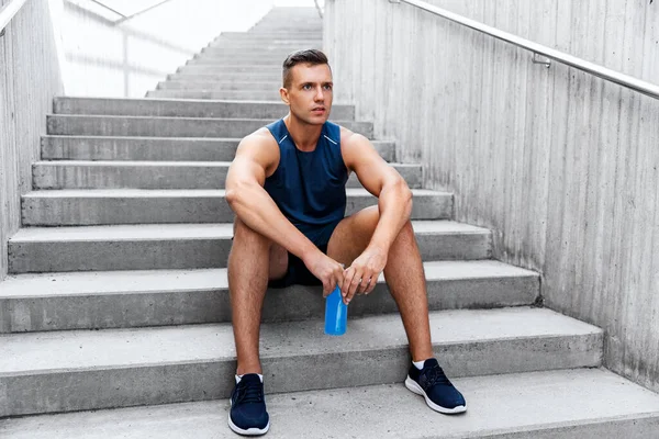 Tired sportsman with bottle sitting on stairs — Stock Photo, Image