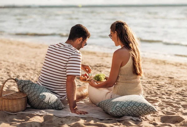 Szczęśliwy para z jedzenie mając piknik na plaży — Zdjęcie stockowe