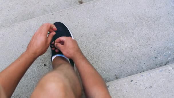 Человек завязывает шнурки на своих кроссовках на улице — стоковое видео