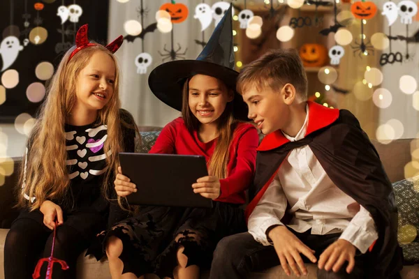 Barn i halloween kostymer med surfplatta dator hemma — Stockfoto
