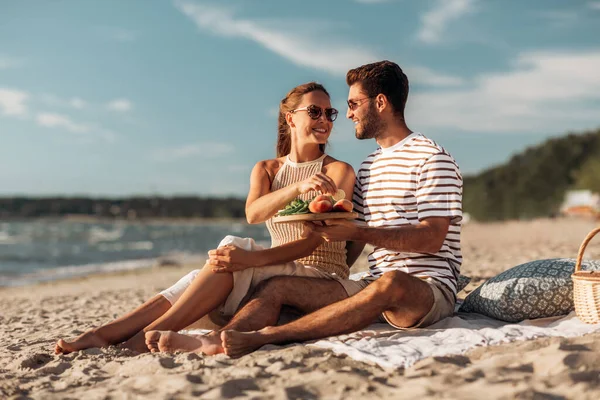 Casal feliz com comida fazendo piquenique na praia — Fotografia de Stock