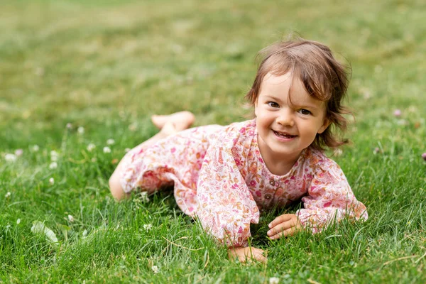 Happy little baby girl lying on grass in summer — Stock Photo, Image