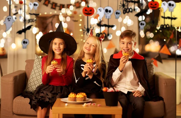 Ungar i halloween kostymer äter cupcakes hemma — Stockfoto