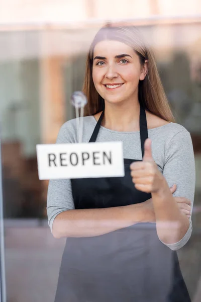 Femme heureuse accrochant bannière rouverte au verre de porte — Photo