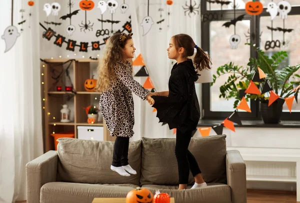 Meninas em trajes de Halloween pulando no sofá — Fotografia de Stock