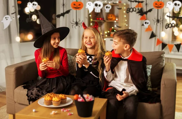 Dzieci w halloween kostiumy jedzące babeczki w domu — Zdjęcie stockowe