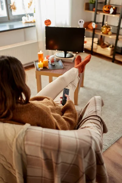 Молода жінка дивиться телевізор вдома на Хеллоуїн — стокове фото