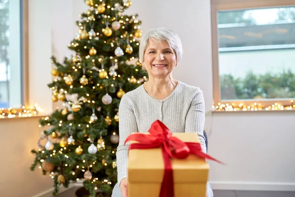 自宅でのクリスマスのギフトを持つ年配の女性の笑みを浮かべてください。 — ストック写真