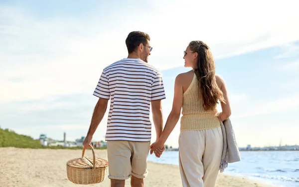 Szczęśliwa para z koszykiem piknikowym spacerująca po plaży — Zdjęcie stockowe