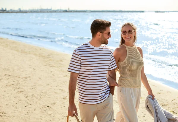 Szczęśliwa para z koszykiem piknikowym spacerująca po plaży — Zdjęcie stockowe