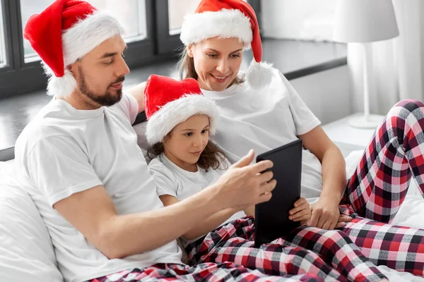 Счастливая семья с планшетным ПК в постели на Рождество — стоковое фото