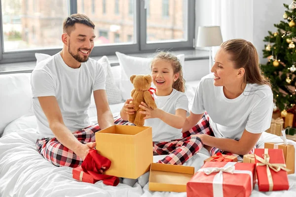 Ευτυχισμένη οικογένεια με χριστουγεννιάτικα δώρα στο κρεβάτι στο σπίτι — Φωτογραφία Αρχείου