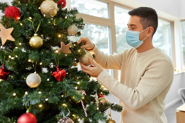 Mann in Maske schmückt Weihnachtsbaum zu Hause Stockbild
