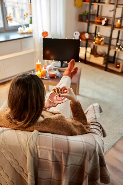 Жінка дивиться телевізор і їсть вафельку на Хеллоуїн — стокове фото