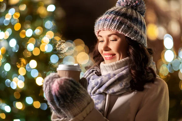 Szczęśliwa kobieta pijąca kawę przy lampkach świątecznych — Zdjęcie stockowe