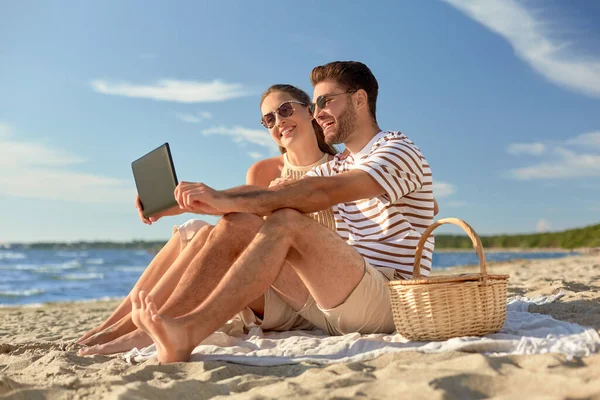 Lyckligt par med surfplatta på picknick på stranden — Stockfoto