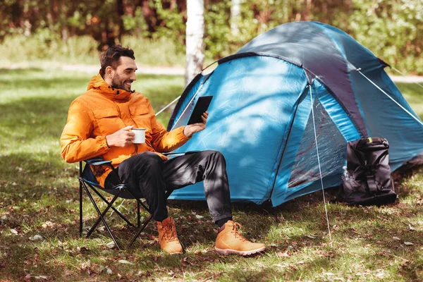 Homem feliz com tablet pc beber chá no acampamento tenda — Fotografia de Stock