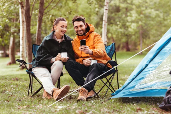 Pareja con teléfono inteligente beber té en el camping — Foto de Stock