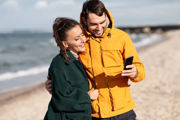 Casal com smartphone na praia de outono — Fotografia de Stock