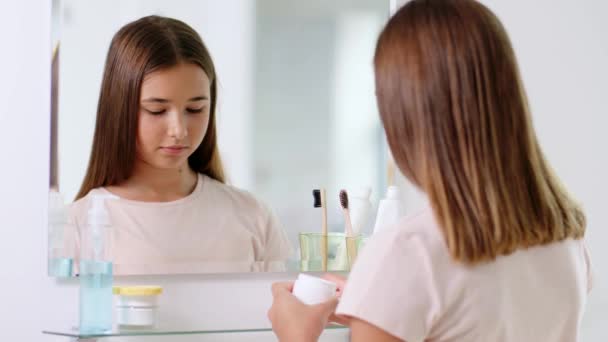 Nastolatka dziewczyna stosując krem nawilżający w łazience — Wideo stockowe