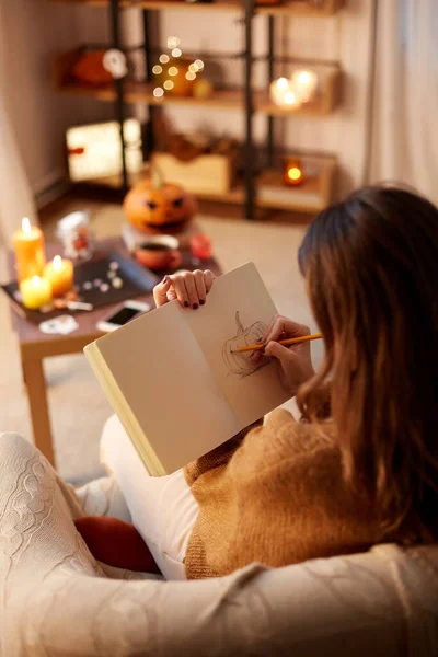 Женщина рисует в альбоме набросков дома на Хэллоуин — стоковое фото
