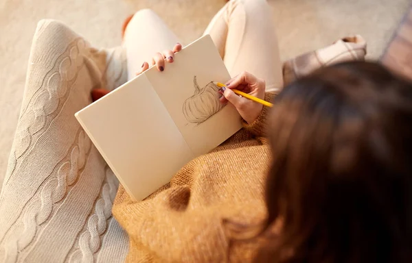 Женщина рисует тыкву в альбоме эскизов дома — стоковое фото