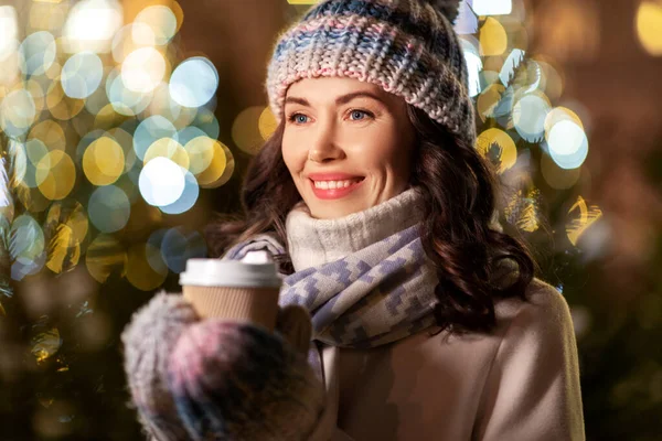 Happy woman drinking coffee over christmas lights — Stock Photo, Image