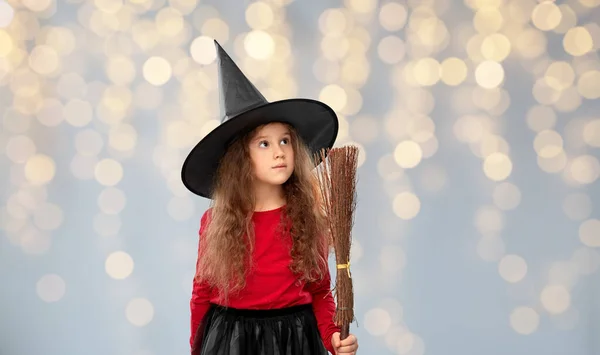 검은 마녀 모자를 쓰고 할로윈에 빗자루를 들고 있는 소녀 — 스톡 사진
