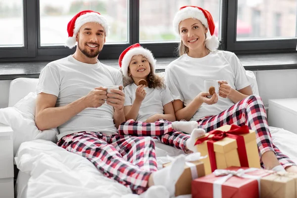 Šťastná rodina jíst sušenky v posteli na Vánoce — Stock fotografie