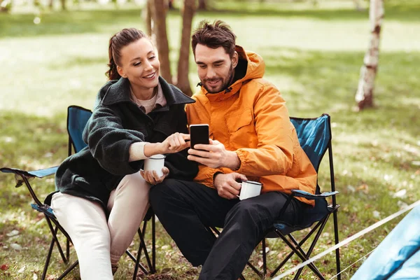 Pareja con teléfono inteligente beber té en el camping —  Fotos de Stock