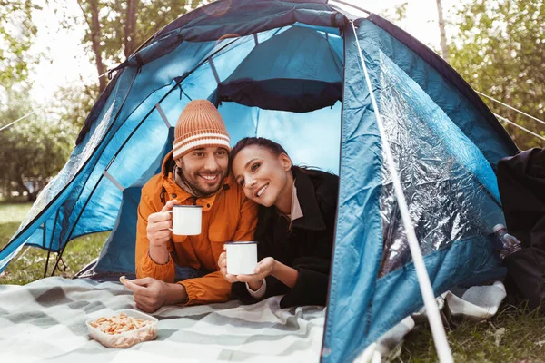 Pareja bebiendo té acostado dentro de la tienda en el camping — Foto de Stock