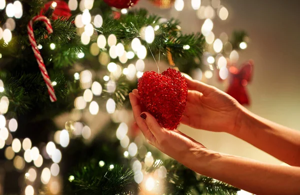 Mãos decorando árvore de natal com coração vermelho — Fotografia de Stock