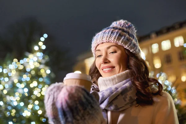 Happy woman drinking coffee over christmas lights — Stock Photo, Image