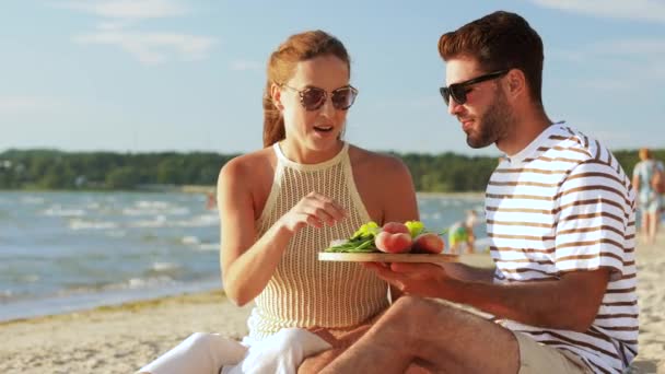 Happy couple with food having picnic on beach — Stock Video