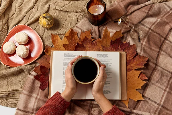 Ruce s šálkem kávy, podzimní listí a knihou — Stock fotografie