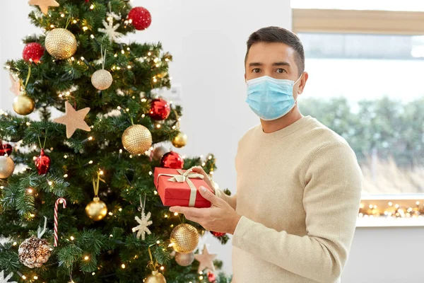 Man in mask with gift at christmas tree at home — Stock Photo, Image